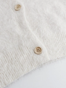 Detail of fluffy knit cardigan fabric with ivory texture and beige round buttons