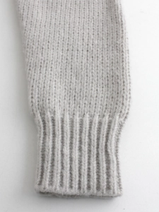 Gros plan d'un gilet gris clair en tricot avec poignets côtelés et texture de tissu doux