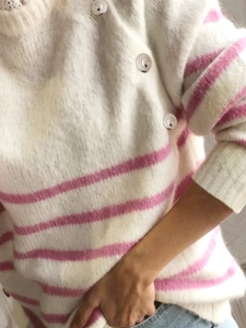 Detailed texture of white knitted sweater with pink stripes and silver buttons on the shoulder