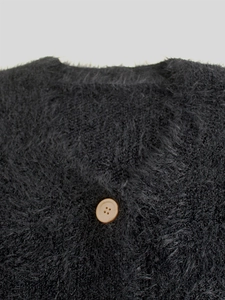Detailed macro view of plush black mohair texture and beige button on knit cardigan