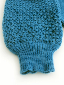 Detailed close-up of peacock blue knit sweater showing waffle texture and ribbed cuffs