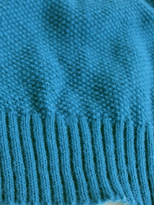 Detailed macro view of blue knit fabric showing pearl stitch texture and ribbed cuff