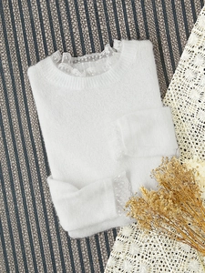 Détail du pull en maille blanche avec bordure en dentelle délicate au col et aux poignets