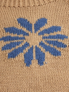 Macro view of blue knit flower pattern and texture on khaki wool pullover sweater