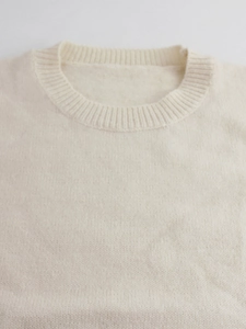 Close-up of a cream crew neck ribbed knit sweater showing fine fabric texture