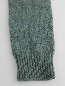 Teal knit sweater close-up showing thick ribbed cuffs and wool blend texture detail