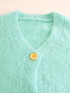 Close-up of mint green plush knit cardigan featuring a V-neckline and yellow button detail