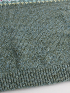 Detail of moss green knit sweater featuring Nordic geometric patterns and ribbed hem