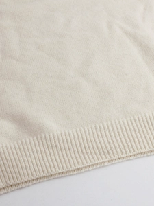 Close-up of premium cream knitted fabric featuring a soft texture and ribbed hem detail
