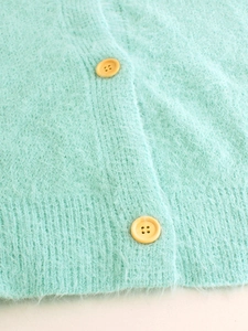 Detailed close-up of fluffy mint green knit cardigan with yellow buttons and ribbed hem