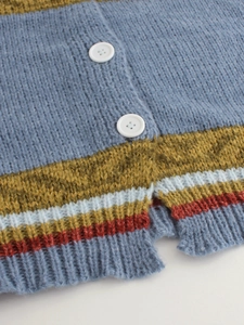 Close-up of a blue knit cardigan with colorful striped hem and white button details