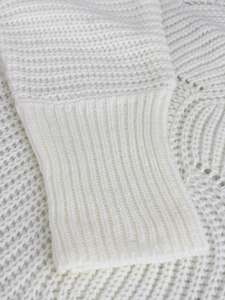 Détail des poignets côtelés et des motifs de tricot ajouré sur le pull en coton blanc