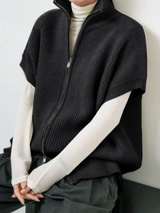Dettaglio di un gilet in maglia nera con cerniera, collo alto e finiture metalliche