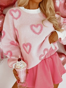 Close-up of pink knit sweater featuring plush heart patterns and white ribbed cuffs