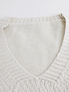 Detailed close-up of cream knit V-neck vest showing ribbed texture and cotton blend fabric