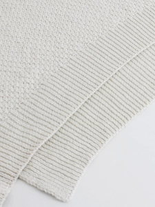 Close-up of cream-colored chunky knit texture and ribbed hem on a V-neck vest