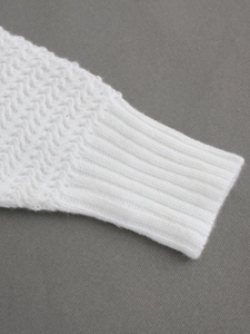 Close-up of white knit sweater cuff featuring herringbone texture and ribbed edges