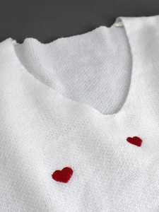Maglione bianco a coste con scollo a V e piccoli cuori rossi ricamati sul petto