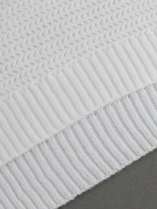 Detail of white chevron knit sweater fabric with ribbed cuffs and intricate texture