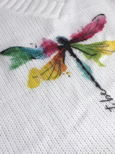 Detail of colorful watercolor dragonfly print and ribbed V-neck on white knitted sweater