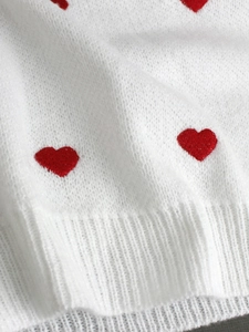 Dettaglio del ricamo a cuore rosso e del bordo a coste su un maglione in maglia bianca