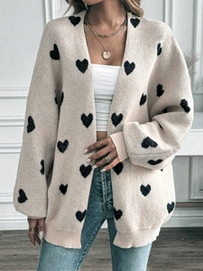 Dettaglio del cardigan in maglia crema con motivi a cuori neri e polsini a coste