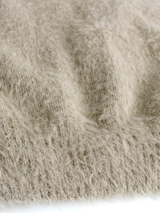 Macro view of beige knit fabric featuring soft mohair-like texture and ribbed cuffs