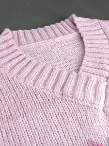 Close-up of the ribbed V-neckline and chunky knit texture of the pink sweater
