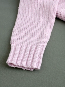 Detail shot of light pink knitted sweater cuffs showing ribbed texture and soft wool blend