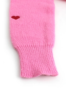 Dettaglio macro di un maglione in maglia rosa con cuore rosso e polsino a coste morbide