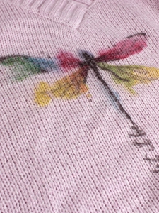 Detail of pink knitted sweater featuring colorful artistic dragonfly pattern texture