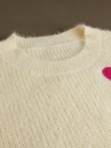 Close-up of fluffy cream knit sweater neckline with a bright pink heart embroidery