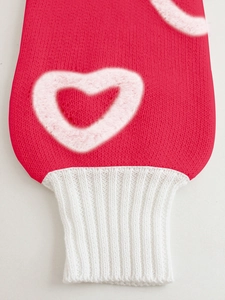 Detail of red knit sweater sleeve with white plush heart pattern and ribbed cuff