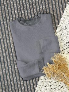 Détail d'un pull en maille gris avec bordure en dentelle délicate au col et aux poignets
