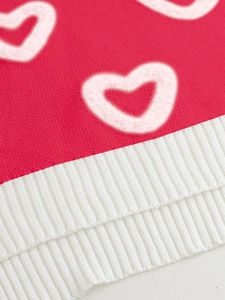 Detailed view of pink knitted fabric featuring fuzzy white heart pattern and ribbed hemline