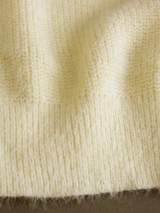 Detailed macro view of soft cream knit sweater featuring premium ribbed texture and plush mohair