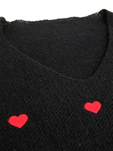 Primo piano del ricamo a cuore rosso sulla trama del maglione nero con scollo a V