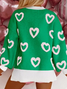Detail of green knit sweater showing pink heart patterns and ribbed white cuffs on sleeve