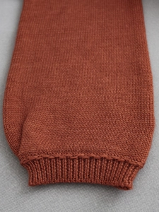 Detailed close-up of brick red knitted sweater cuff with ribbed knit texture