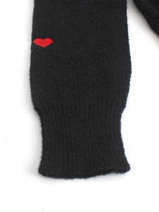Dettaglio del polsino di un maglione in maglia nera con ricamo a cuore rosso