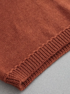 Macro detail of rust red knit sweater fabric showing uniform texture and ribbed cuffs