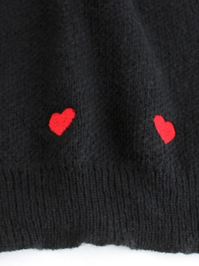 Dettaglio di maglione nero in maglia con ricami a cuore rosso e bordo a costine