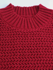 Close-up of a red knit sweater showing detailed honeycomb texture and ribbed neckline