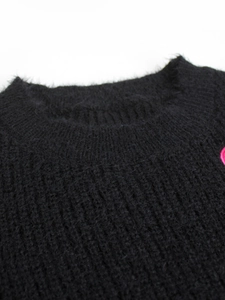 Close-up of soft black fuzzy knit sweater fabric with pink heart patch detail