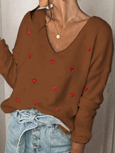 Dettaglio maglione in maglia marrone con scollo a V, motivi a cuore rossi e trama a coste