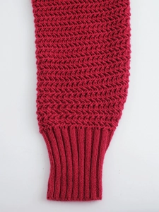 Detailed close-up of rose red knitted sweater cuff with herringbone texture and ribbed edges