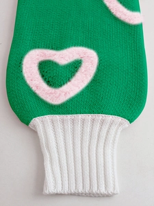 Detailed view of green knit sweater sleeve with pink fuzzy heart pattern and ribbed cuff