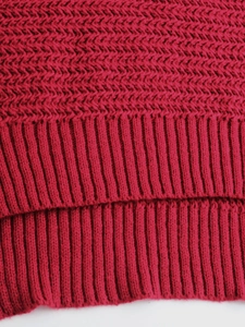 Detail shot of dark red knit sweater featuring herringbone pattern and ribbed hem texture