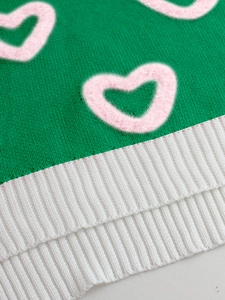 Detail of green knit sweater showing pink fuzzy heart patterns and white ribbed hem