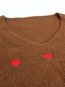 Dettaglio maglione in maglia marrone con scollo a V e ricamo a cuore rosso sul petto